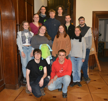 Ein Bild von jungen Menschen, die auf einem Gruppenbild auf einer hölzernen Treppe im Innenraum stehen