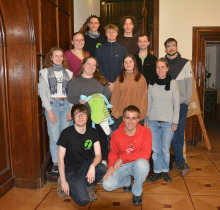 Ein Bild von jungen Menschen, die auf einem Gruppenbild auf einer hölzernen Treppe im Innenraum stehen